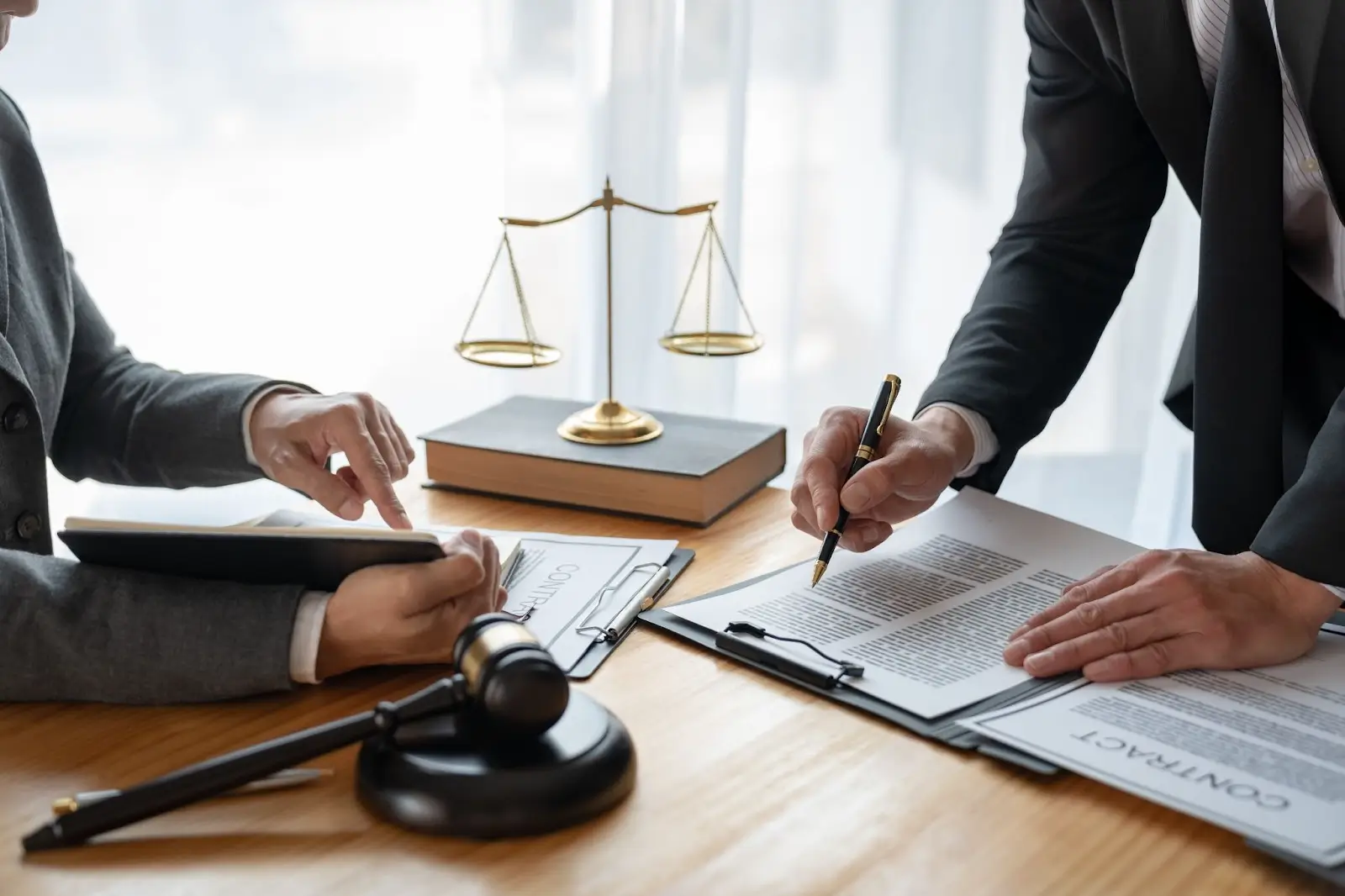 closeup of two people signing a contract with gavel and pendulum on desk