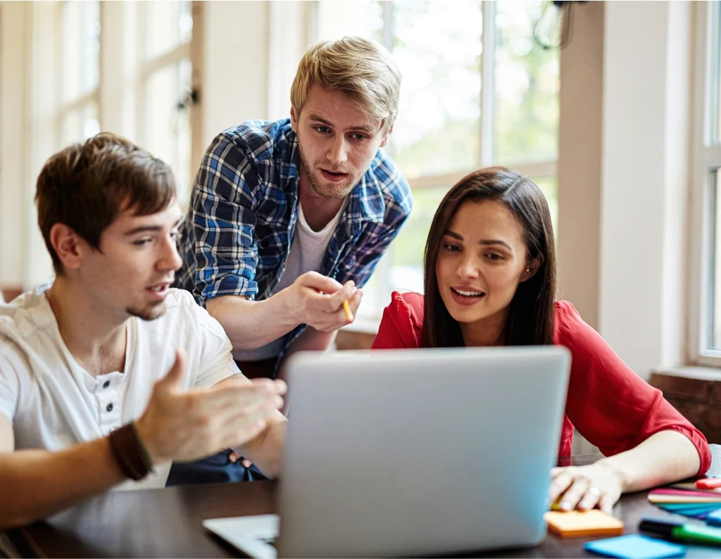 3 students pointing at laptop in classroom