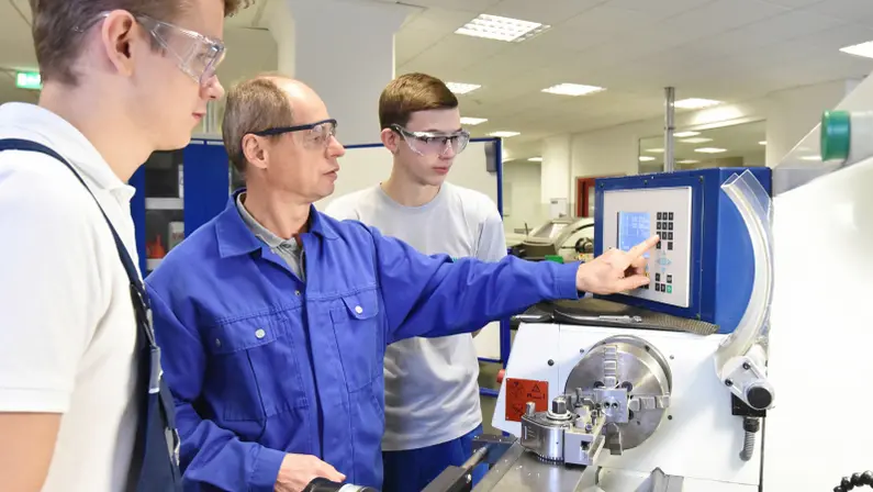 Young trainees in technical vocational training are taught by older trainers on a CNC lathe